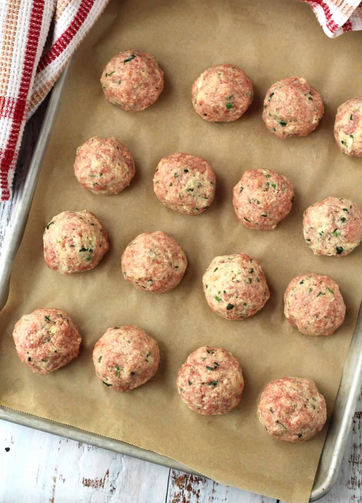 Peas and mozzarella stuffed raw meatballs on baking sheet.