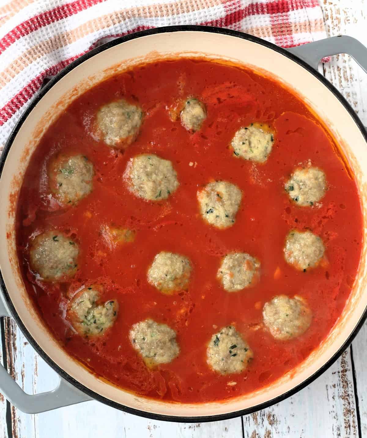 Sicilian stuffed meatballs simmering in tomato sauce in large sauce pan.