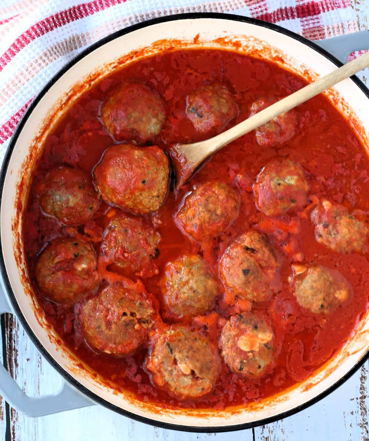 Stuffed Sicilian meatballs simmering in tomato sauce in large skillet.