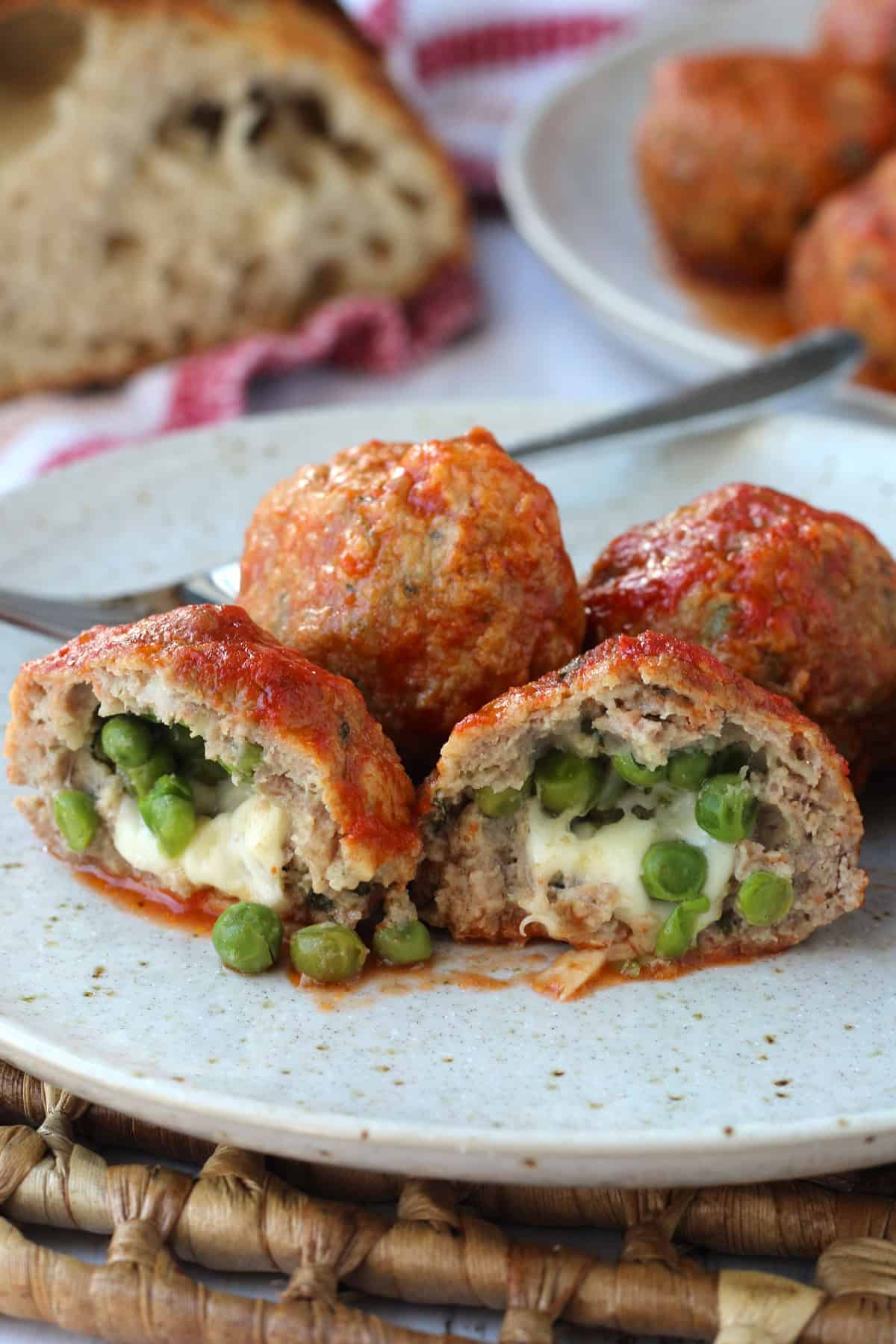 Sicilian stuffed meatballs with mozzarella and peas cut open on plate with more meatballs and sliced bread.