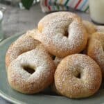 Ciambelline di ricotta (ricotta ring cookies) on blue plate with glass of milk behind them.