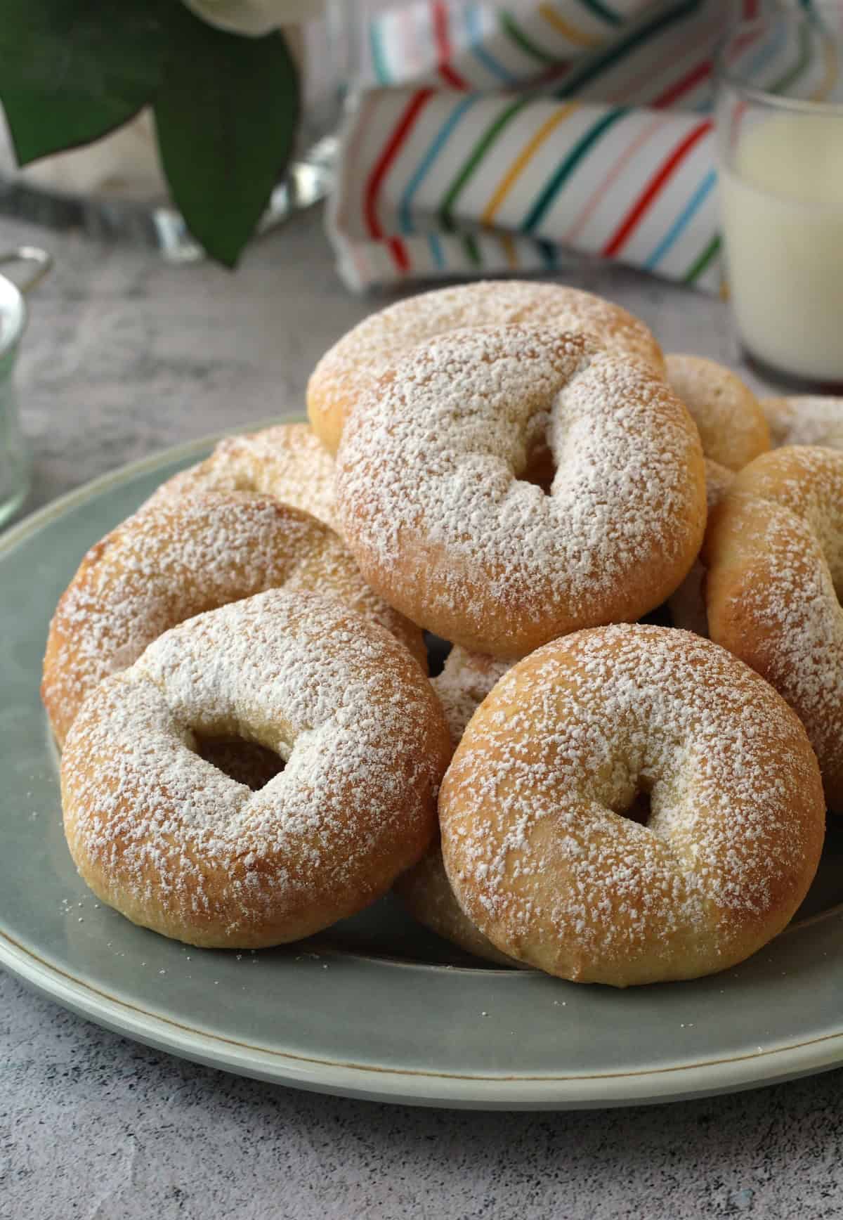 Ciambelline di ricotta (ricotta ring cookies) on blue plate with glass of milk behind them.