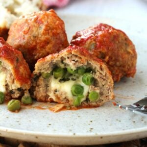 Peas and mozzarella stuffed meatballs cut open on plate.