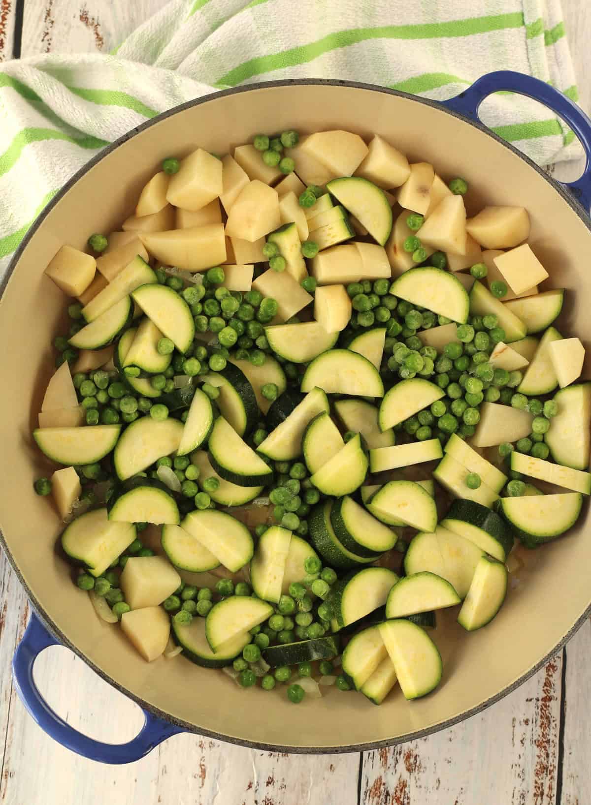 Large skillet filled with zucchini, potatoes and peas.