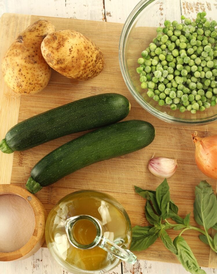 Bowl of peas, zucchini, potatoes, onion, garlic clove, basil leaves, olive oil and salt