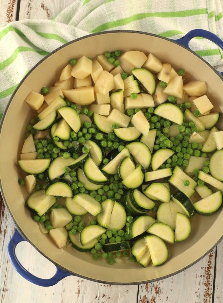 Stewed zucchini with potatoes and peas in large blue skillet