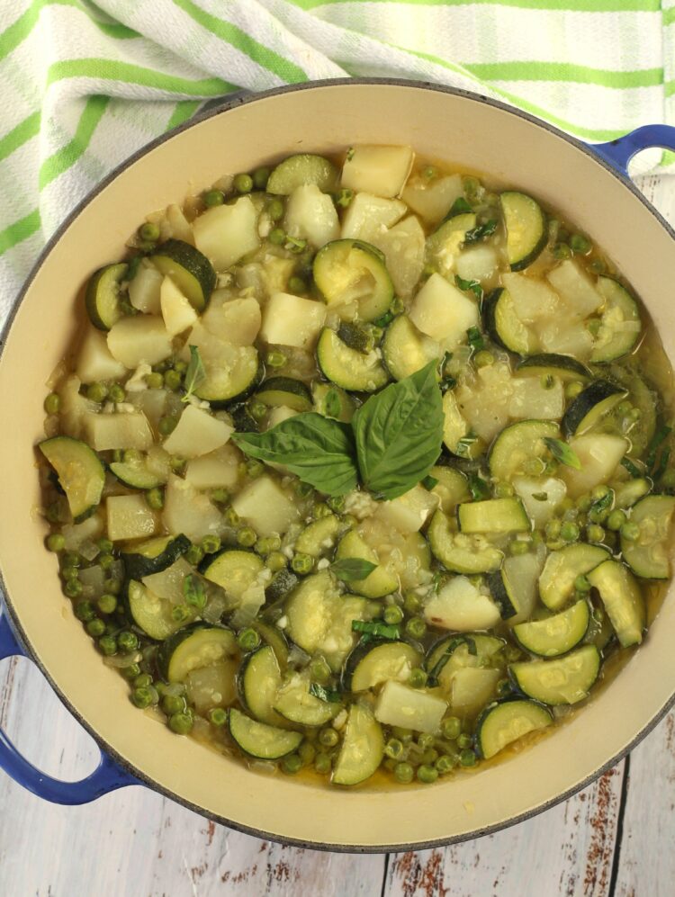 Stewed zucchini with potatoes and peas topped with basil in blue skillet.