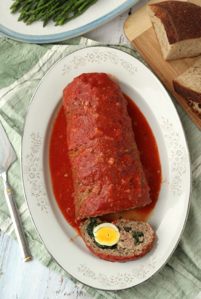 Overview of tomato sauce covered meatloaf stuffed with egg and spinach cut open on oval plate.