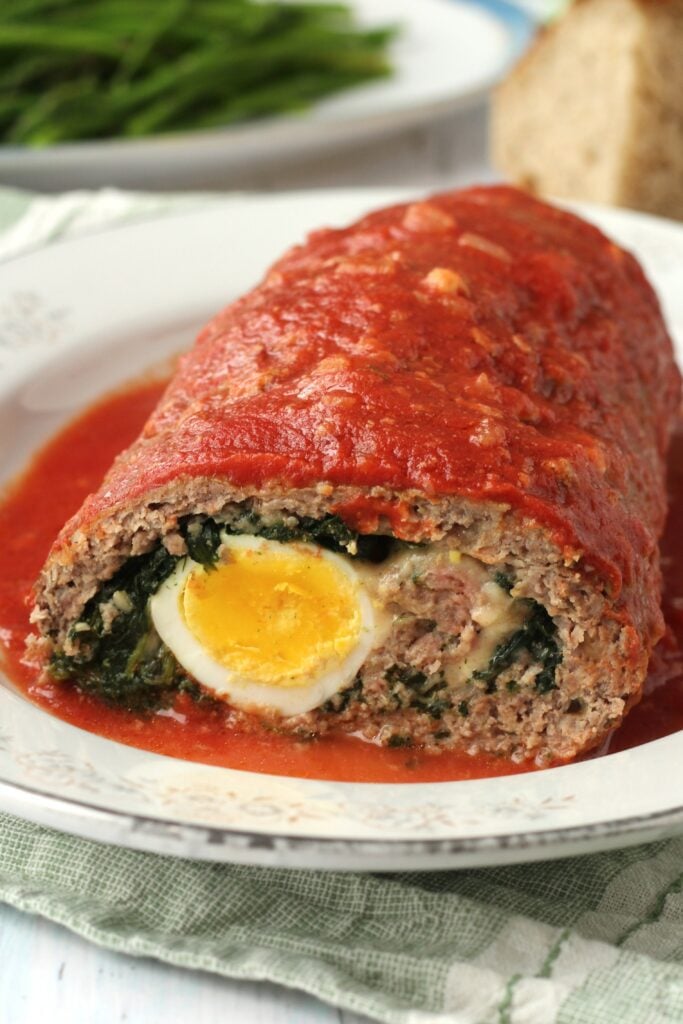 Meatloaf stuffed with egg and spinach in tomato sauce sliced open on plate.