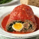 Meatloaf stuffed with hardboiled eggs and spinach cut open on plate.