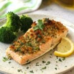 Baked salmon with breadcrumbs, lemon and garlic on plate with lemon wedge and broccoli.