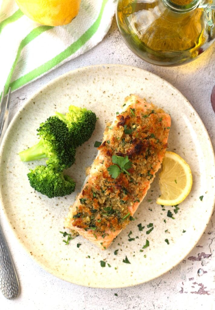 Crispy baked salmon with breadcrumbs plated with lemon wedge and broccoli.