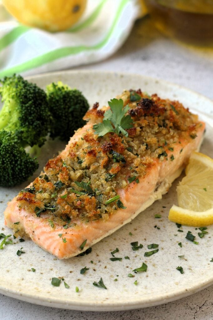 Salmon with breadcrumb topping on plate with lemon wedge and broccoli florets.