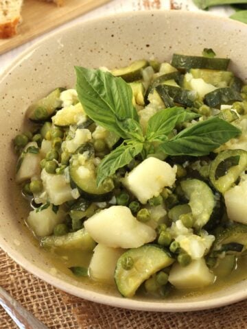 Bowl of stewed zucchini with potatoes and peas and basil.
