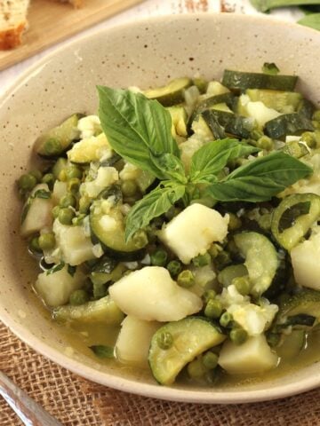 Zucchini stew with potatoes and peas topped with fresh basil in bowl.