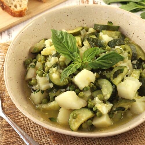 Zucchini stew with potatoes and peas topped with fresh basil in bowl.