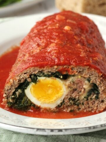 Stuffed meatloaf with hard boiled eggs and spinach in tomato sauce cut open on plate.