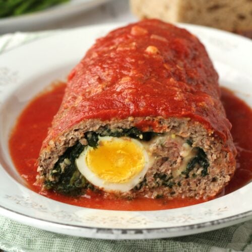 Stuffed meatloaf with hard boiled eggs and spinach in tomato sauce cut open on plate.