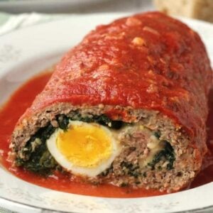 Spinach and egg stuffed meatloaf in tomato sauce cut open on plate.