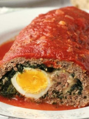 Spinach and egg stuffed meatloaf in tomato sauce cut open on plate.