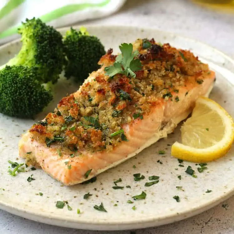 Baked salmon with breadcrumbs plated with lemon wedge and broccoli.