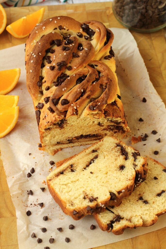 Chocolate chip brioche bread sliced on wood board with chocolate chips and orange wedges.