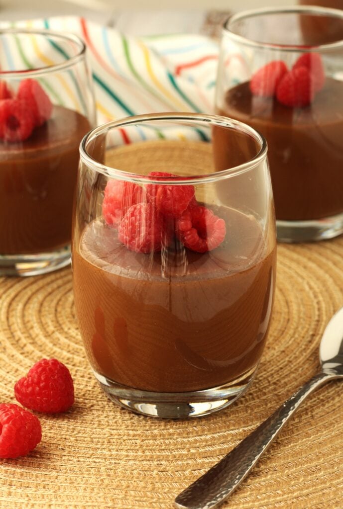 Glass of almond milk chocolate pudding topped with raspberries.