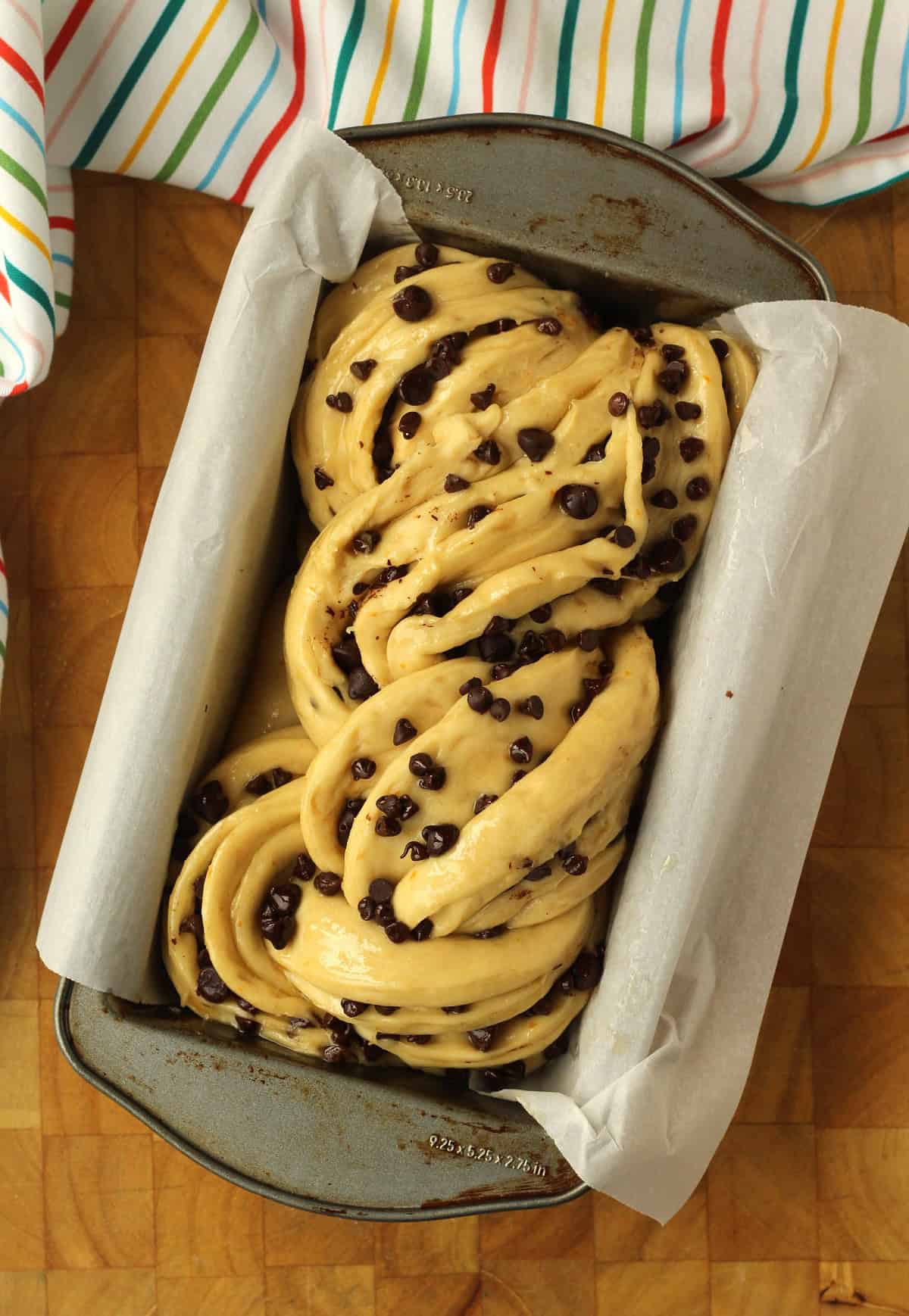 Proofed chocolate chip brioche bread in loaf pan covered with parchment paper.