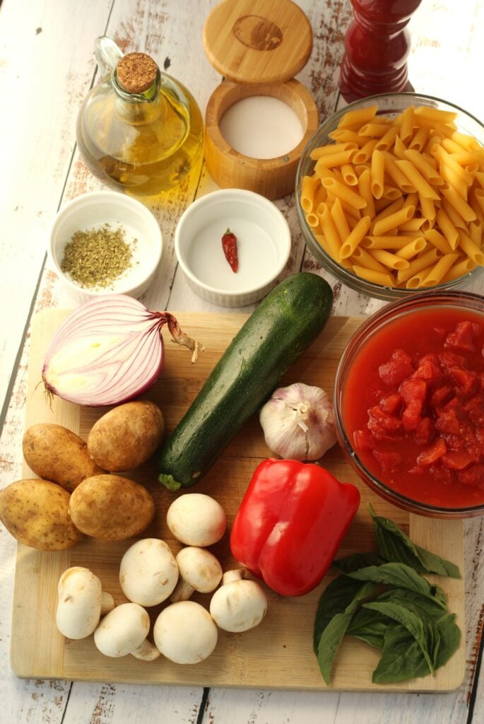 Bowl of pasta, tomato sauce, basil, vegetables and seasoning for veggie pasta dish.