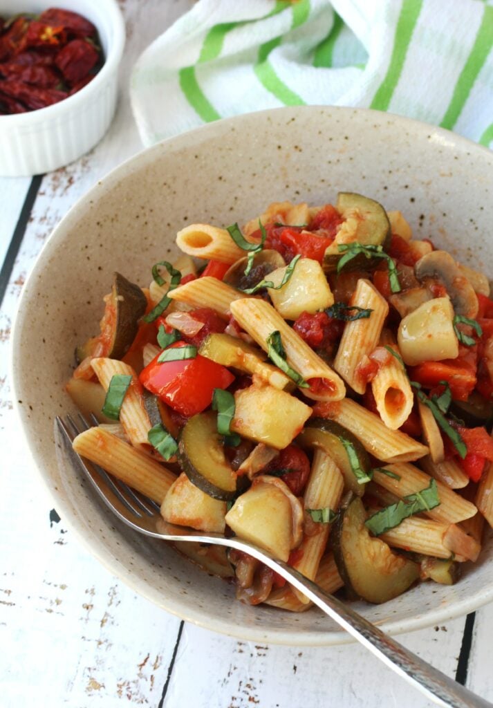 Bowl with pasta with vegetables and tomato sauce with fork in it.