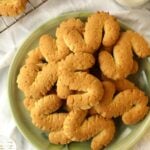 S shaped cookies piled on plate with cooling rack with cookies on side.
