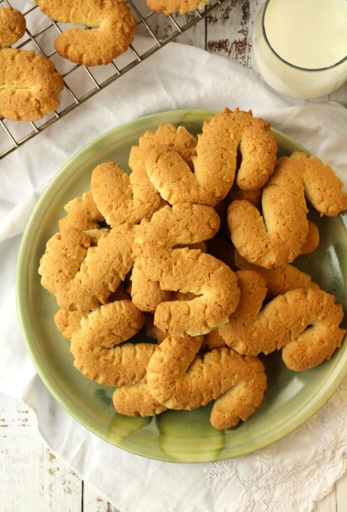 S shaped cookies piled on plate with cooling rack with cookies on side.