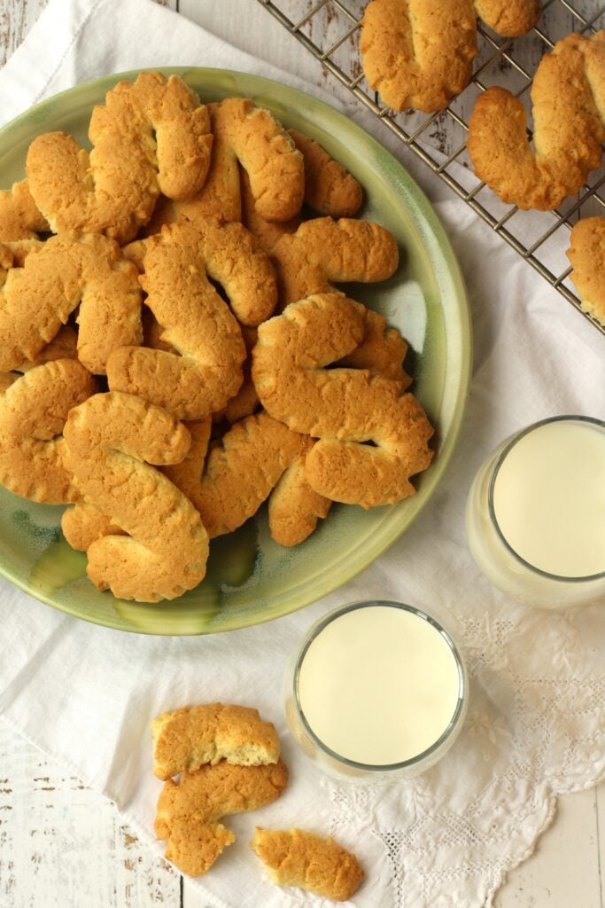 S shaped cookies piled on plate alongside glasses of milk and cookie in pieces.
