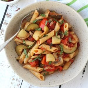 Pasta with vegetables and tomato sauce in bowl with fork.