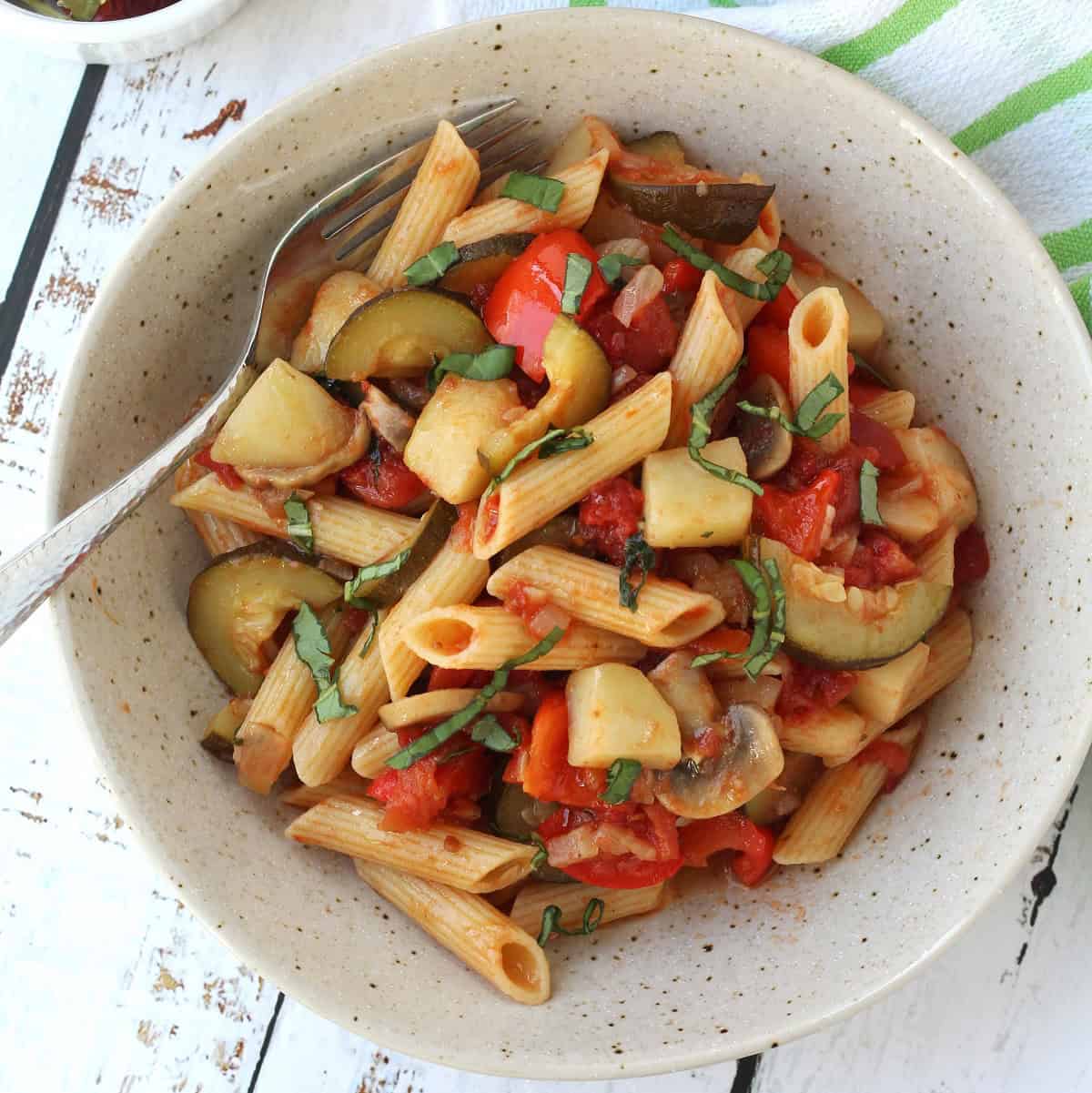 Pasta with vegetables and tomato sauce in bowl with fork.