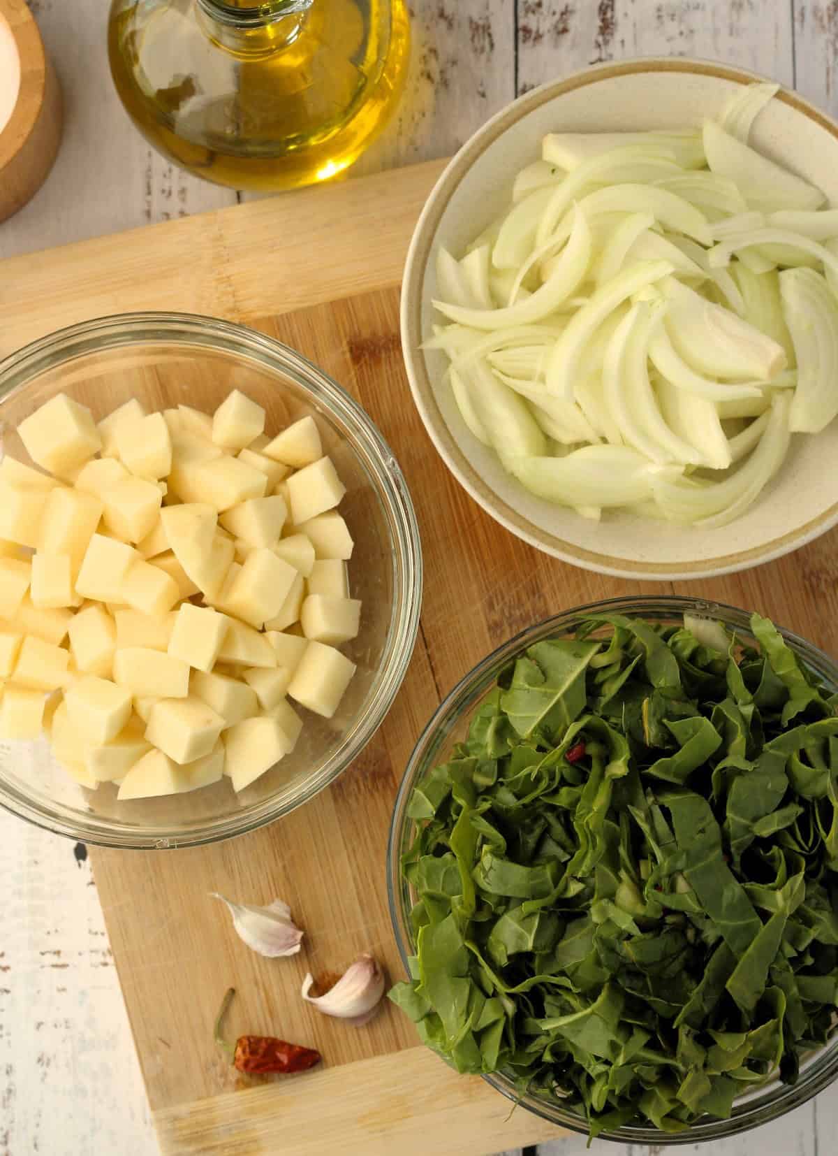 Bowls with sliced onion; chopped swiss chard; cubed potatoes; garlic and olive oil bottle.