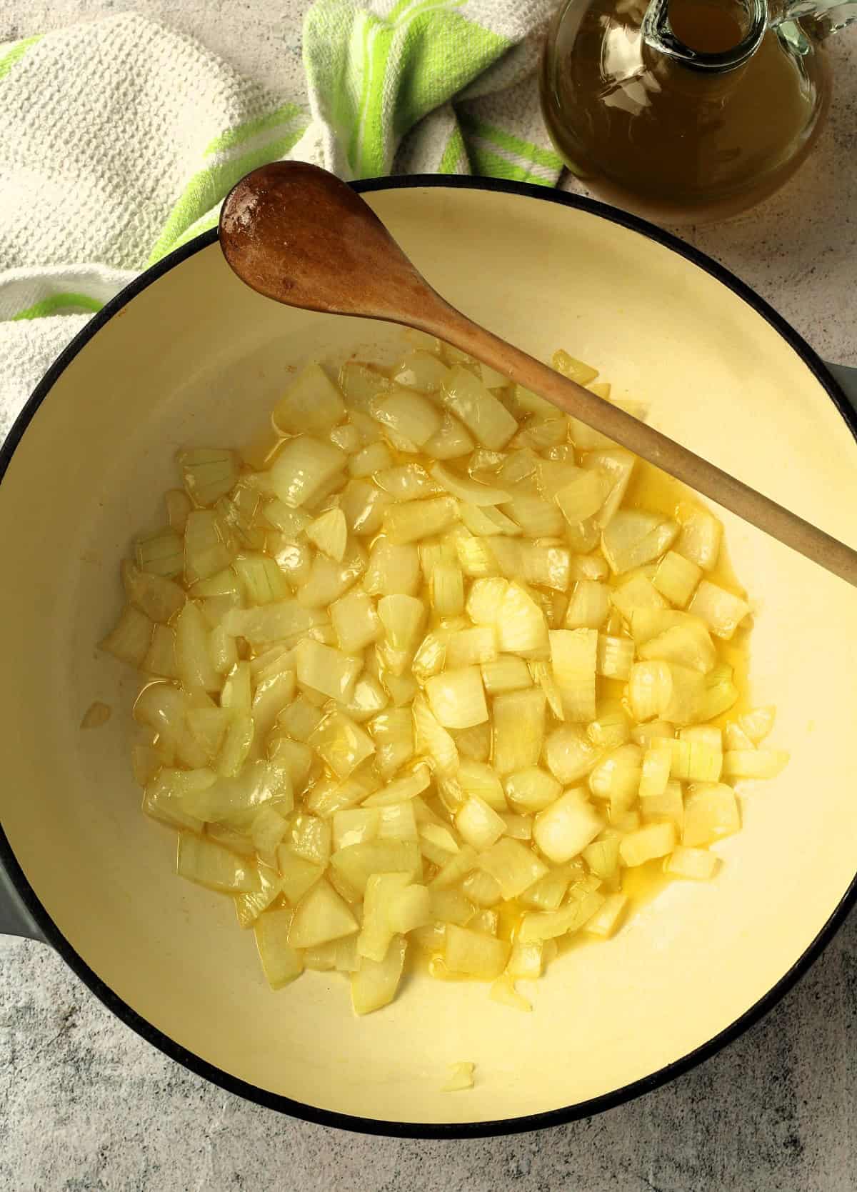 Diced onions sautéed in skillet with olive oil and wooden spoon resting on it.