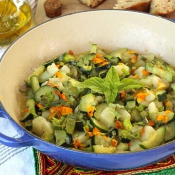 Sautéed zucchini flowers with zucchini and potatoes in skillet with olive oil and bread around it.