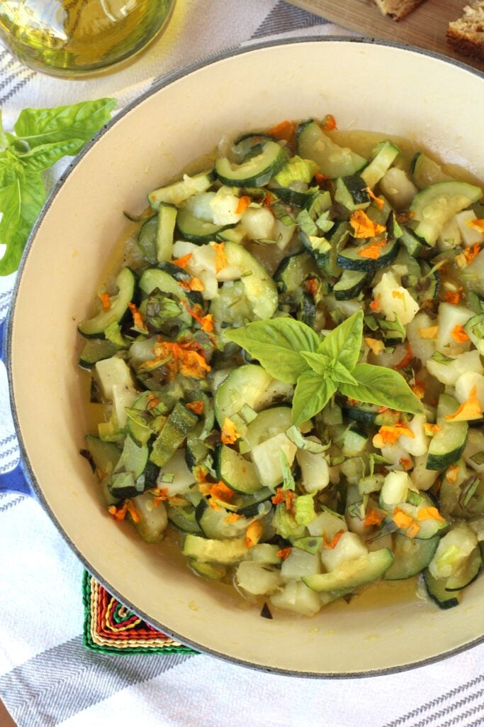 Skillet filled with zucchini, potato and zucchini blossom sauté topped with basil.