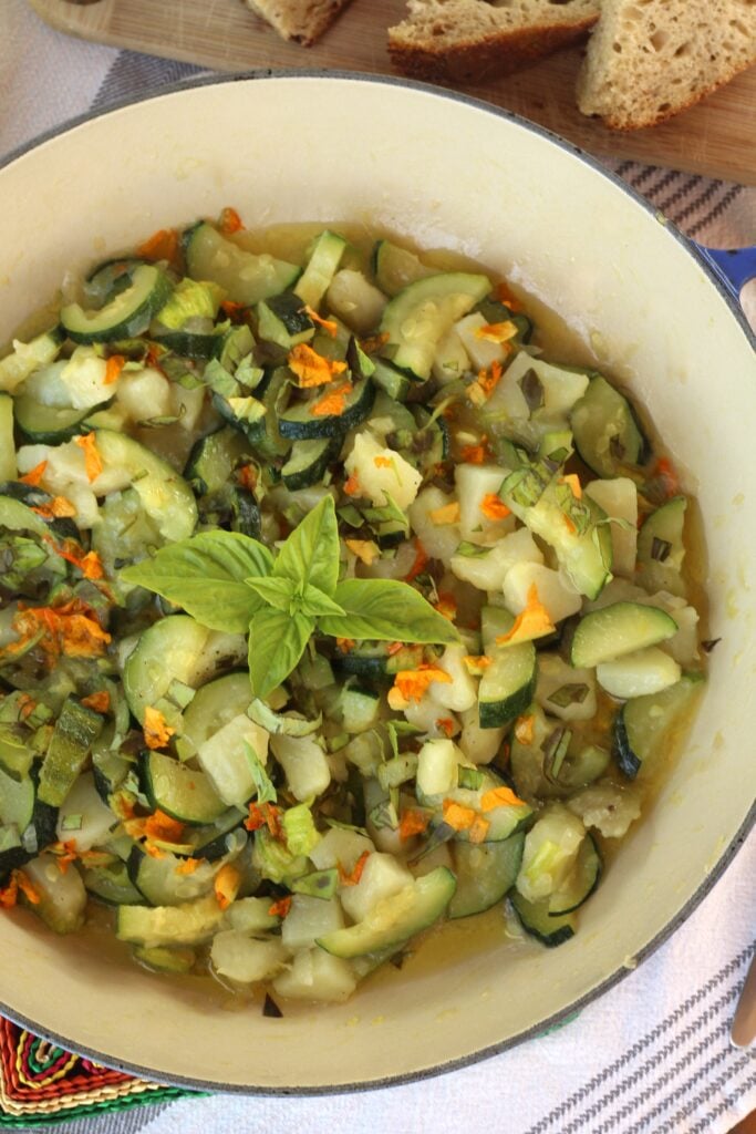 Skillet filled with zucchini, potatoes and zucchini flowers with basil.