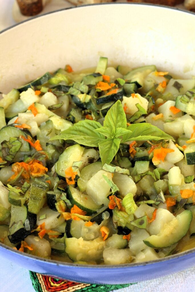 Blue skillet filled with sautéed zucchini flowers, zucchini and potato topped with basil.