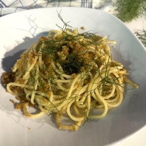 Wild fennel pasta topped with fennel fronds on white plate.