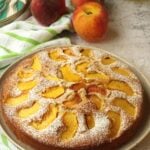 Peach cake with olive oil on plate surrounded by peaches and olive oil bottle.