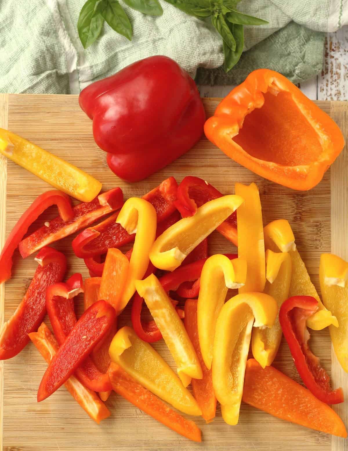 Red and orange peppers on wood board cut into strips.