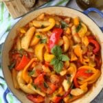 Skillet with Italian stewed peppers with potatoes and tomatoes with bread slices behind it.