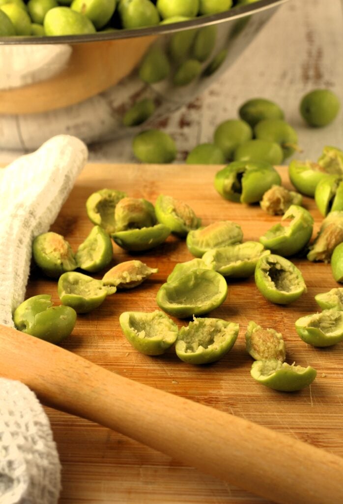 Cracked green olives with a meat mallet on wood board, pits removed.