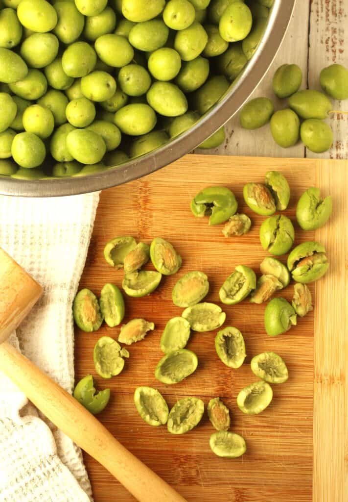 Sicilian green olives cracked on wood board with meat mallet.