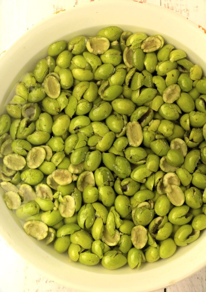 Cracked green olives in bowl submerged with water.