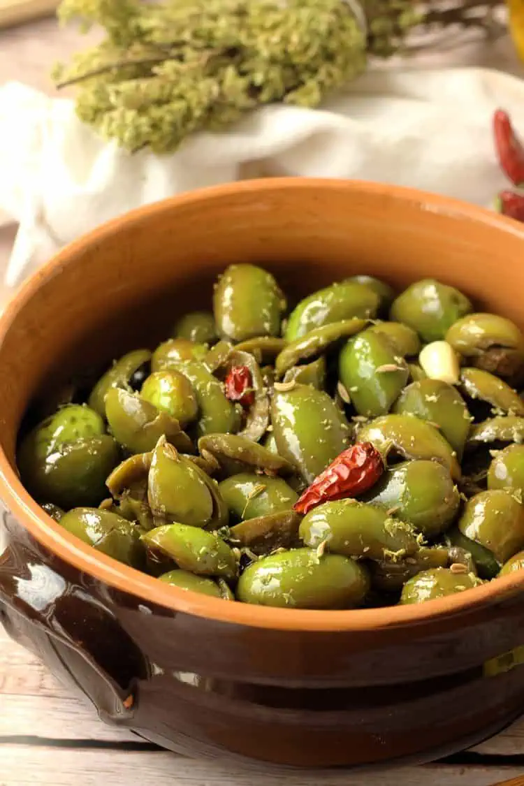 Sicilian cracked olive salad in ceramic bowl surrounded by oregano branches.
