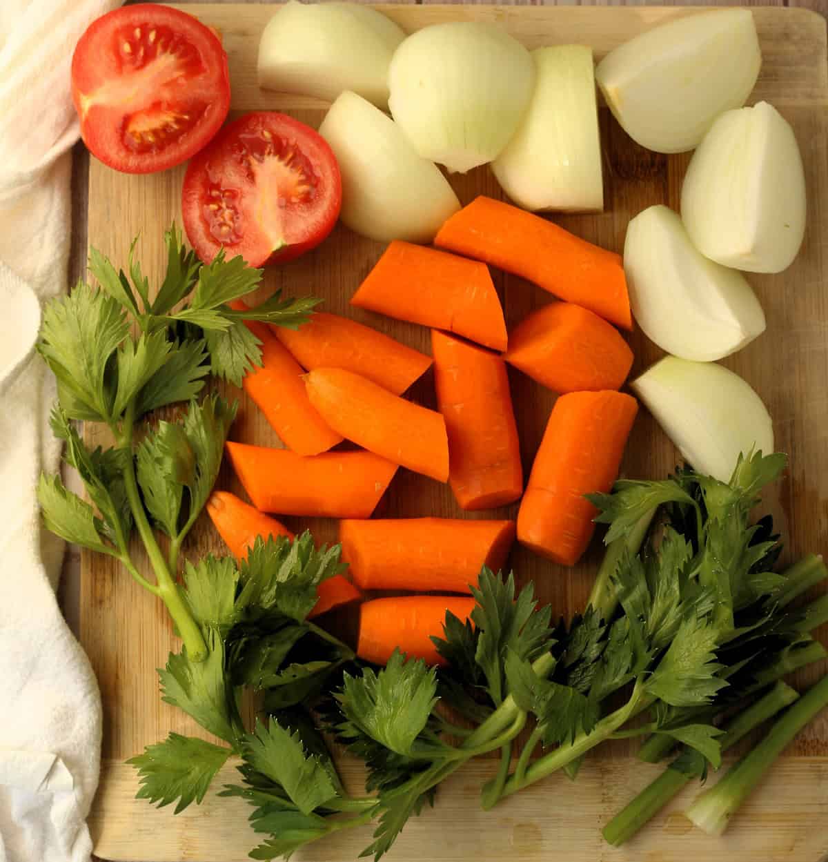 Chopped carrots, onions, tomato, and celery stalks with leaves.